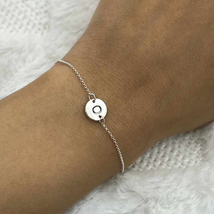 Pulsera de plata con la letra O en la mano