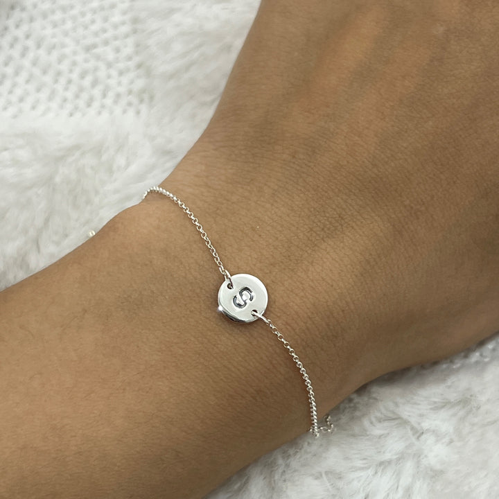 Pulsera de plata con la letra S usando en la mano